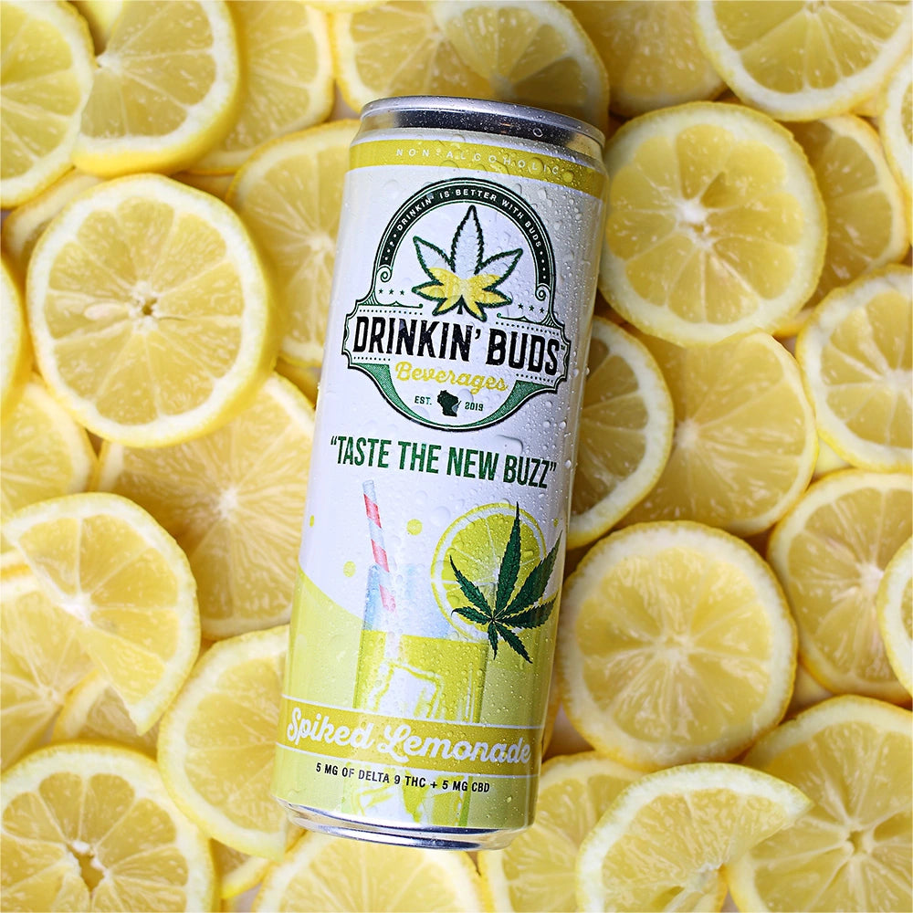 A chilled can of Drinkin’ Buds Spiked Lemonade rests on a vibrant bed of freshly sliced lemons, emphasizing its citrusy and refreshing flavor.