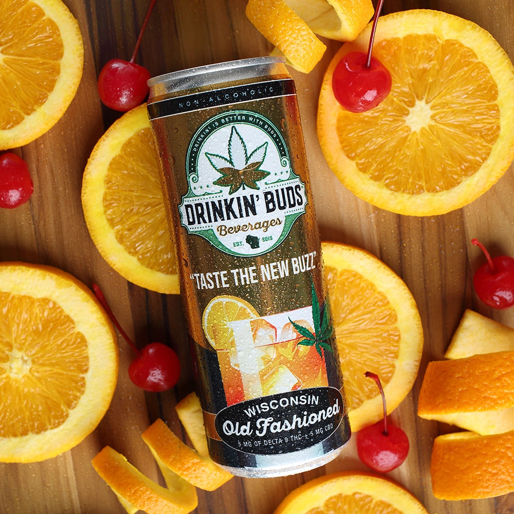 A chilled can of Drinkin’ Buds Wisconsin Old Fashioned rests on a wooden surface surrounded by fresh orange slices, cherries, and curled orange peels, highlighting its classic cocktail-inspired flavor.