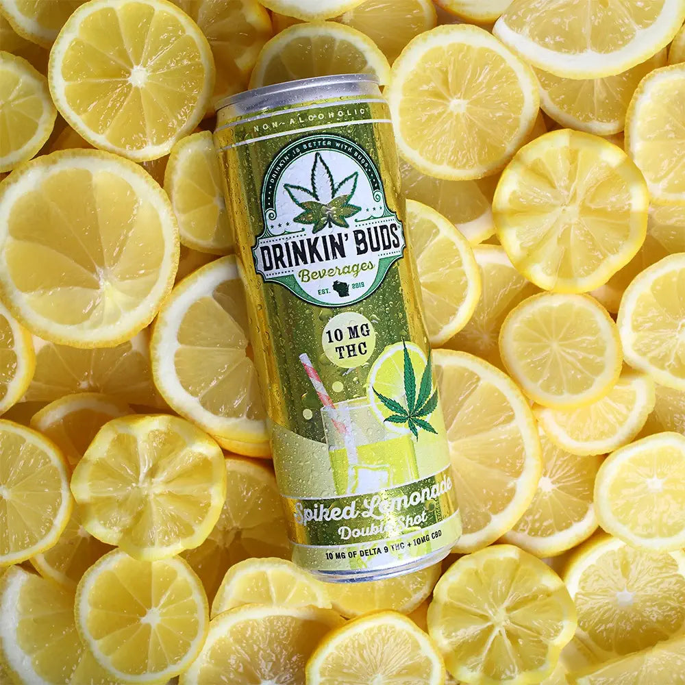A can of Drinkin’ Buds Spiked Lemonade, a THC-infused non-alcoholic beverage, rests on a vibrant background of sliced lemons.