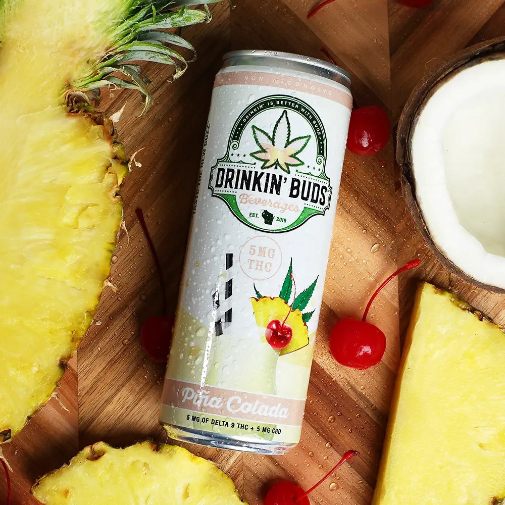 
                      
                        Can of 'Drinkin' Buds' Pina Colada on a wooden surface with pineapple and cherries.
                      
                    